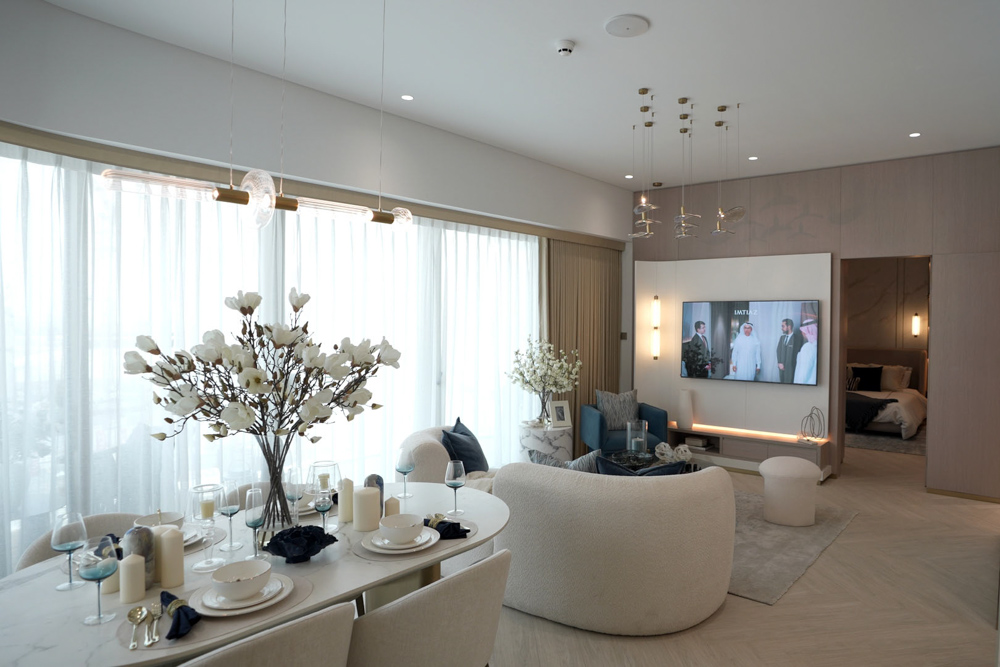 Beach Walk Residence A modern living room with a dining area, elegant decor, large windows, and a TV featuring three men in suits.